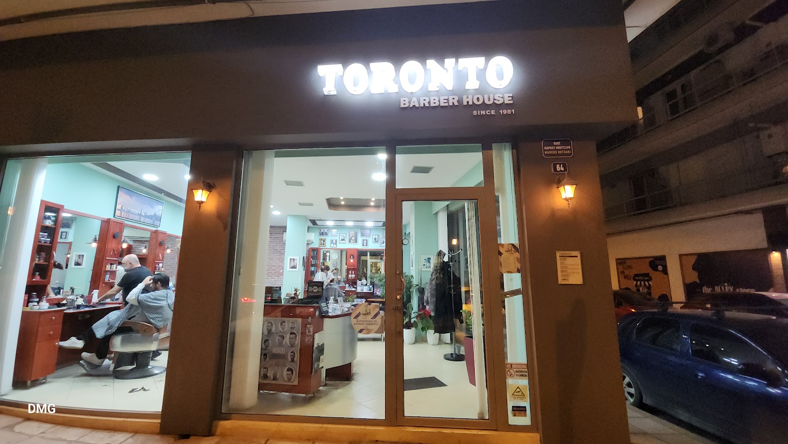 Η φωτισμένη πινακίδα Toronto Barber House στη Μαρκ. Μπότσαρη 64, στη Θεσσαλονίκη, το βράδυ